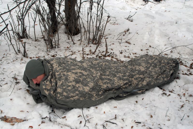 Một người đàn ông sử dụng túi ngủ quân đội ngoài trời tiết